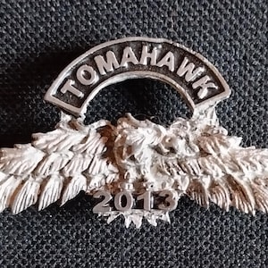 May include: Silver metal pin with a stylized eagle design and the words "Tomahawk 2013" on it.