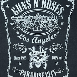 May include: Black patch featuring the Guns N' Roses logo in white. The design includes the band's name, a skull with guns, roses, and the text "Los Angeles" and "Paradise City". The patch is bordered by a barbed wire design.