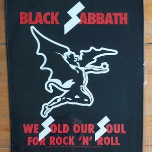 Puede incluir: Parche de Black Sabbath con el nombre de la banda en rojo y un gráfico blanco de una figura alada. El texto "WE SOLD OUR SOUL FOR ROCK 'N' ROLL" también está en rojo. El parche está sobre un fondo negro.