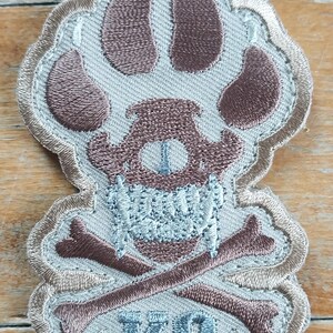 May include: Tan embroidered patch with a brown paw print, skull, crossbones, and the text "K9".