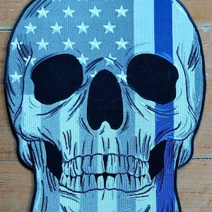 May include: A blue and white skull patch with a thin blue line down the right side. The skull is designed to look like the American flag.
