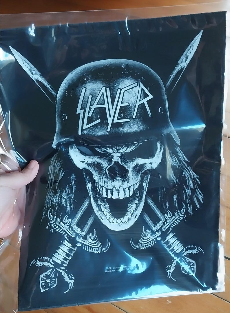 May include: Black and white graphic print featuring a skull wearing a helmet with the word "SLAYER" across the front. Two crossed swords are behind the skull. The image is on a black background.