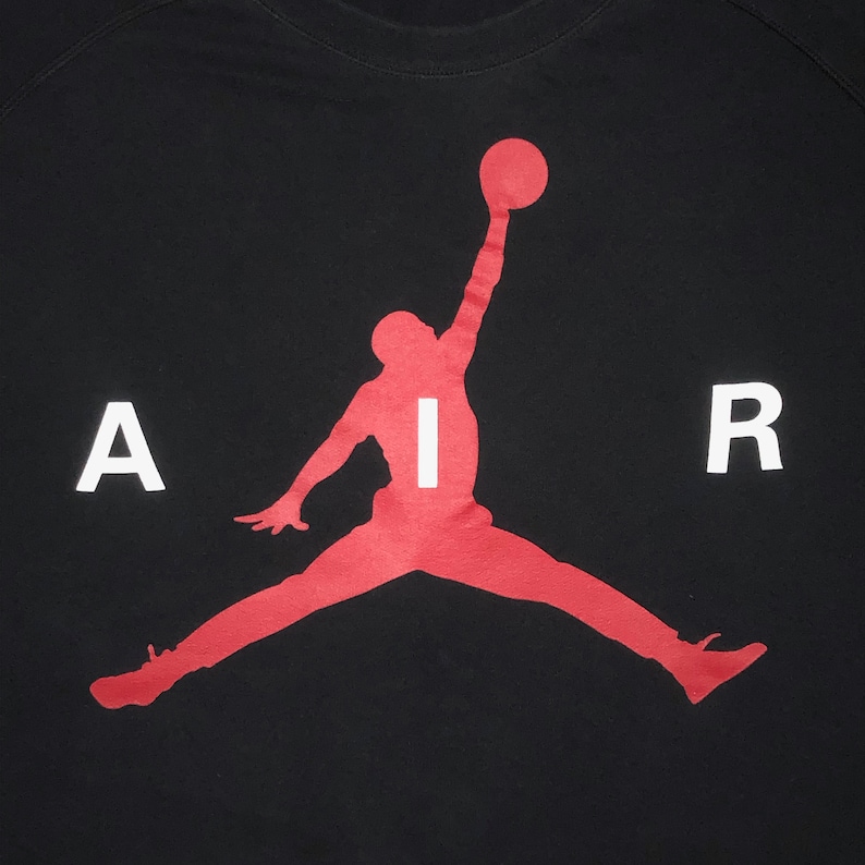 May include: Black t-shirt featuring a red silhouette of a basketball player performing a slam dunk. The word "AIR" is written in white across the player's silhouette.