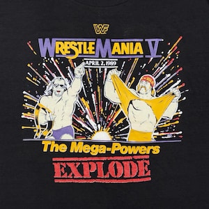 Könnte beinhalten: Schwarzes T-Shirt mit einem farbenfrohen Grafikdesign für Wrestlemania V. Der Text "WrestleMania V" ist in Lila und Gelb gehalten. Das Bild zeigt zwei Wrestler und die Worte "The Mega-Powers EXPLODE" in Rot.
