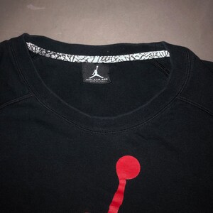 May include: Black t-shirt with a red Jumpman logo and a white tag that says "Nike Air Jordan" on the front.