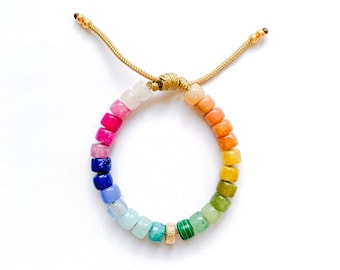 May include: A rainbow-colored beaded bracelet with a gold-colored adjustable closure. The bracelet features a variety of square-shaped beads in shades of pink, red, blue, green, yellow, and orange. The bracelet is displayed on a white background.