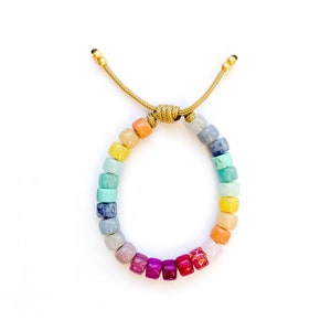 May include: A rainbow colored beaded bracelet with a gold clasp. The beads are square shaped and are arranged in a gradient pattern from orange to red.