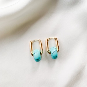 May include: Gold hoop earrings with a turquoise blue stone accent. The earrings are on a white background.