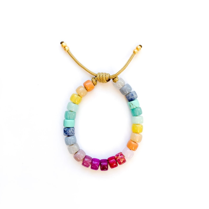 May include: A rainbow colored beaded bracelet with a gold clasp. The beads are square shaped and are arranged in a gradient pattern from orange to red.