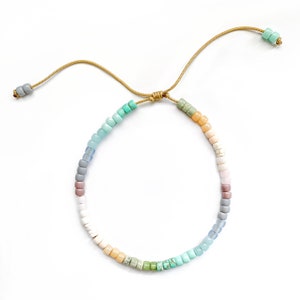 May include: A colorful beaded bracelet with a light brown cord. The beads are in shades of blue, green, white, and pink.