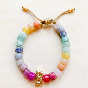 May include: A rainbow beaded bracelet with a gold letter "B" charm. The beads are in shades of blue, green, yellow, orange, pink, and purple.
