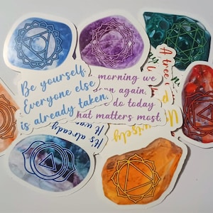 May include: A set of seven colorful stickers with chakra symbols and inspirational quotes. The quotes include "Be yourself", "Everyone else is already taken", "Morning we do again", "What matters most", "It's already happening", and "A tree is a tree".
