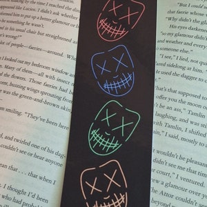 May include: Four colorful smiling masks with stitched mouths and X's for eyes. The masks are red, blue, green, and pink. The background is black.