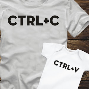 以下が含まれることがあります： 黒い文字で「CTRL+C」と書かれた白いTシャツと、黒い文字で「CTRL+V」と書かれた白いベビーロンパースです。