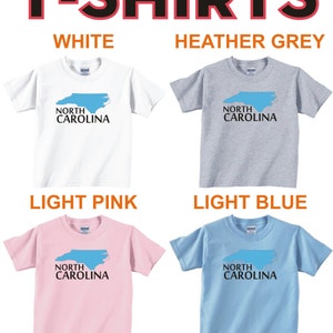 May include: Four t-shirts with the text "NORTH CAROLINA" and an outline of the state of North Carolina in blue. The shirts are white, heather grey, light pink, and light blue.