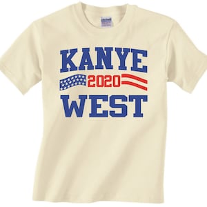 May include: A beige t-shirt with a blue and red graphic print that says "Kanye 2020 West" with an American flag design.