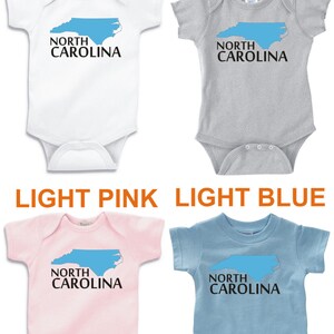 May include: Four baby bodysuits with a North Carolina outline and the text "North Carolina". The bodysuits are in white, heather grey, light pink, and light blue.