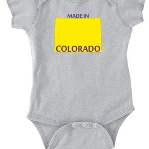 May include: Gray baby onesie with a yellow rectangle and the text "MADE IN COLORADO" in blue and red.