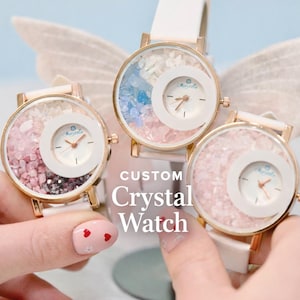 May include: Three custom crystal watches with white straps and gold-coloured cases. The watch faces are filled with colourful crystals and have a smaller, white, circular dial. The text "CUSTOM Crystal Watch" is visible.