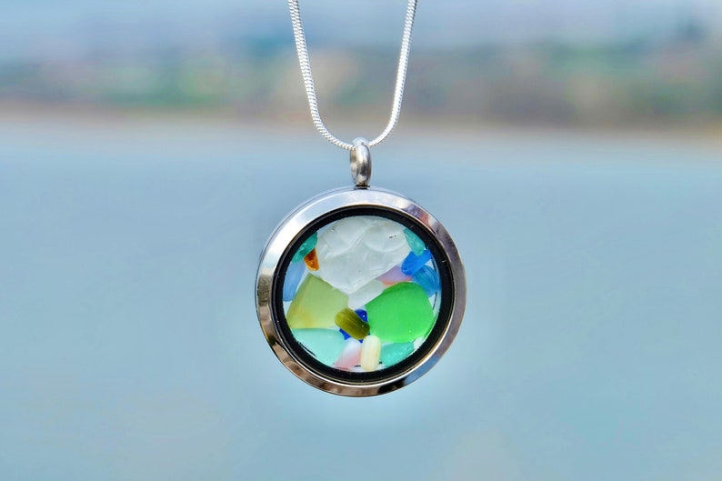 May include: A silver locket necklace with a round glass pendant filled with colorful sea glass pieces.