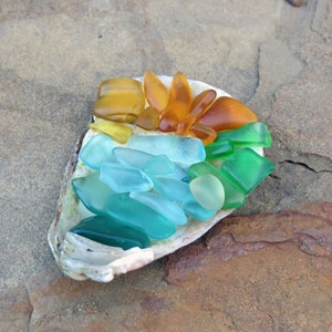 May include: A seashell filled with colorful sea glass in shades of green, blue, and amber. The sea glass is arranged in a rainbow pattern.