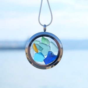 May include: A silver locket necklace with a clear glass insert containing small pieces of sea glass in shades of blue, green, and yellow.