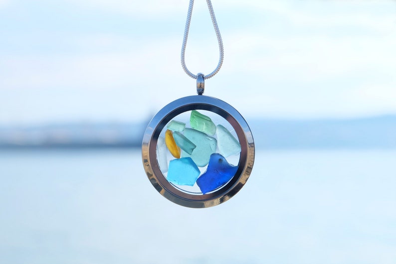 May include: A silver locket necklace with a clear glass insert containing small pieces of sea glass in shades of blue, green, and yellow.