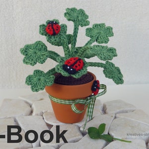 Peut inclure: Plante verte en crochet avec des feuilles de trèfle à quatre feuilles dans un pot en terre cuite avec un ruban vert et blanc. Trois coccinelles rouges sont sur la plante. Le texte "E-Book" est au premier plan.