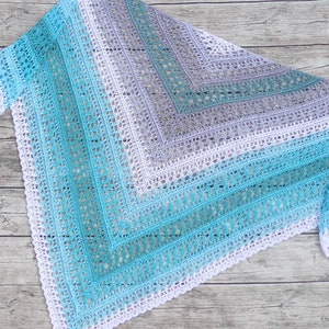 May include: A crocheted shawl in a gradient of turquoise, teal, and light grey with a white crocheted border.