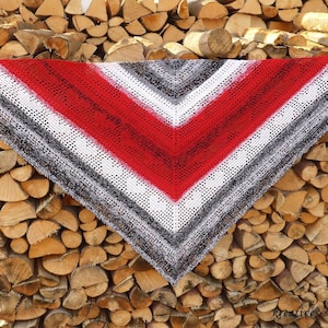 May include: A triangular crocheted shawl with a red, white and grey ombre design. The shawl is draped over a pile of stacked firewood.