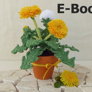 May include: A crocheted dandelion plant in a terracotta pot, with bright yellow and white flower heads, green leaves, and a yellow ribbon. The image includes the text "E-Book".