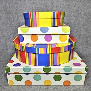 May include: A stack of four colorful gift boxes. The bottom box is white with large polka dots in red, blue, and yellow. The next box is striped in red, yellow, blue, and green. The third box is white with large polka dots in red, blue, and yellow. The top box is yellow with red, blue, and green stripes.