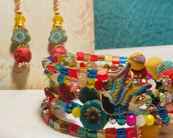 May include: Colorful beaded bracelet with a bird charm and matching dangle earrings. The earrings have yellow, blue, and red beads. The bracelet features a variety of beads in red, green, blue, and yellow. The earrings and bracelet are handmade.