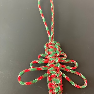 Könnte beinhalten: Handgefertigter Weihnachtsbaumschmuck aus rotem, grünem und weißem Paracord. Das Baumdesign hat eine Schlaufe zum Aufhängen und aufwendige Knoten. Eine festliche Dekoration für die Weihnachtszeit.