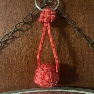 May include: A red paracord keychain with a knotted ball at the end. The keychain is attached to a silver key ring.