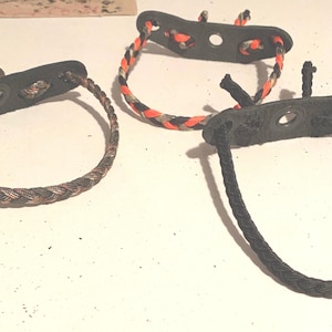 May include: Three different styles of bow release aids. One is black with a camouflage pattern, one is black with a red and black pattern, and one is black with a black and white pattern.