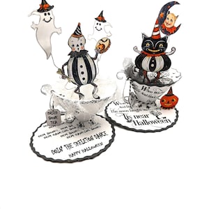 May include: Halloween-themed decorations featuring a black cat in a teacup, ghosts, and a skeleton figure. The decorations include text that reads "Doin' the Skeleton Dance" and "Tis near Halloween". The figures are in black, white, and orange.