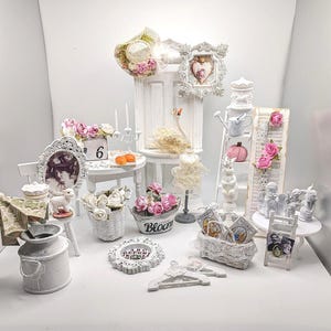 May include: A collection of miniature decorative items including a white milk can, a basket with pink flowers, a small mannequin, a white ladder shelf with a pink pumpkin, a framed heart image, a white chair, and various small figurines and accessories.