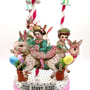 May include: A carousel-themed centerpiece featuring children riding spotted rabbits. The circular base is decorated with pink sequins and a sign reading FREE BUNNY RIDES. The structure includes striped poles with green and white canopy tops.