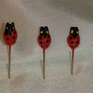 May include: Three red and black ladybug-shaped pins with yellow spots and silver stems.