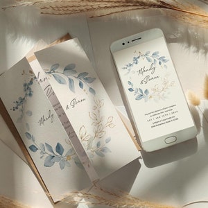 Puede incluir: Una invitación de boda plegada con un diseño de acuarela de hojas azules y doradas. La invitación está sobre un fondo blanco con los nombres "Mandy & Simon" escritos en cursiva. La invitación está junto a un teléfono inteligente blanco con un diseño similar en la pantalla.
