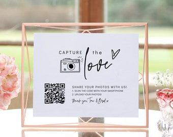 Könnte beinhalten: Ein weißes Schild mit schwarzem Text und einem QR-Code. Der Text lautet "Capture the love" mit einem Kamera- und Herzsymbol. Der Text lautet auch "Teilen Sie Ihre Fotos mit uns! 1. Scannen Sie den Code mit Ihrem Smartphone 2. Laden Sie Ihre Fotos hoch! Vielen Dank, Toui & Budo x".