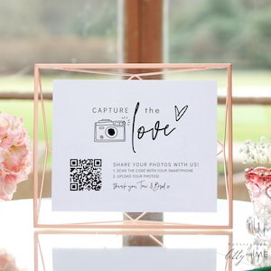 Puede incluir: Un cartel blanco con texto negro y un código QR. El texto dice "Capture the love" con un icono de cámara y corazón. El texto también dice "¡Comparte tus fotos con nosotros! 1. Escanea el código con tu teléfono inteligente 2. Sube tus fotos! Gracias, Toui & Budo x".