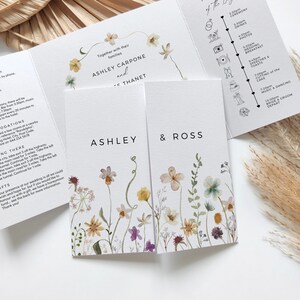 May include: A wedding invitation with a floral design. The invitation features the names Ashley Carpone and Ross Thanet, along with a timeline of the wedding day. The invitation is printed on white cardstock and has a watercolor floral design.