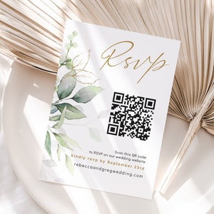 Puede incluir: Una tarjeta RSVP blanca con una fuente de escritura dorada en cursiva que dice "RSVP". Un código QR en blanco y negro está en el centro de la tarjeta. El texto debajo del código QR dice "Escanea este código QR para responder en nuestro sitio web de bodas por favor responde antes del 23 de septiembre rebeccaandgregwedding.com".