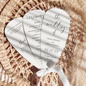 May include: Three white wedding ceremony programs tied with a white ribbon. The programs have black text with the words "ceremony" and "the wedding of" visible. The date "06.07.29" is also printed on the program.