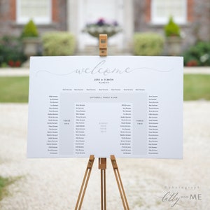 Puede incluir: Un cartel de boda blanco con el texto "welcome" en letra cursiva. El cartel enumera los nombres de los invitados bajo los títulos "Table One", "Kindly Find Your Seat" y "Table Two".