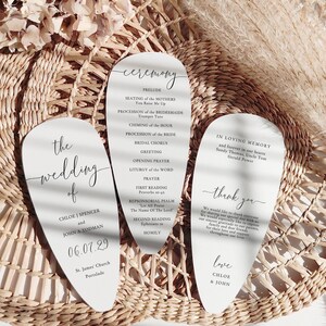 May include: Three white wedding ceremony cards with curved tops, featuring elegant calligraphy. The cards include the wedding details, ceremony order, and a thank you message. The cards are arranged on a woven basket.