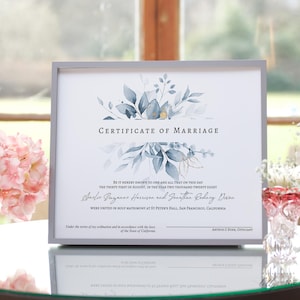 May include: A certificate of marriage with a watercolor floral design in shades of blue and gold. The text reads "Certificate of Marriage" and includes the names "Anclee Guzanne Harrison" and "Jonathan Rodney Dixon". The document is framed in a gray frame.
