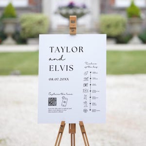 May include: A white wedding sign with black text and icons. The sign reads "TAYLOR and ELVIS 08.07.20XX" and includes a timeline of the day's events. A QR code is included with the text "Capture the love" and instructions to scan the code to upload photos to a shared album.
